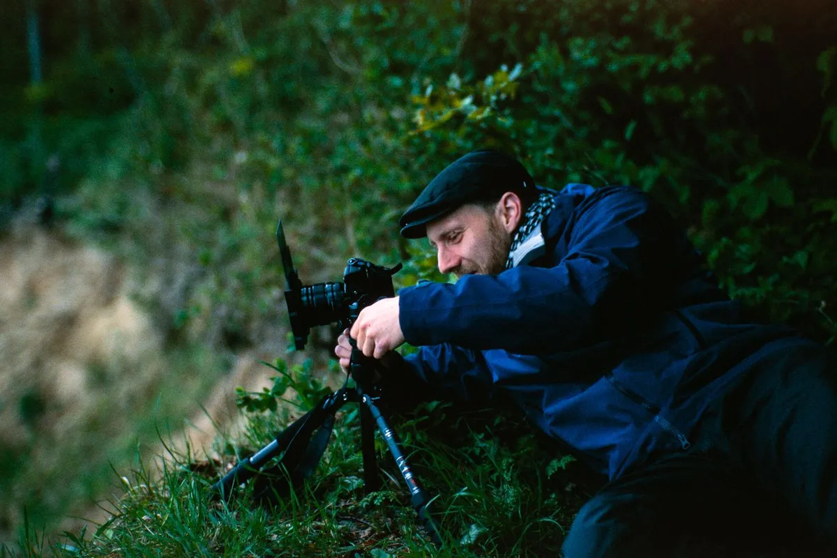 konrad im grünen liegend am stativ mit kamera bei einem fotoworkshop