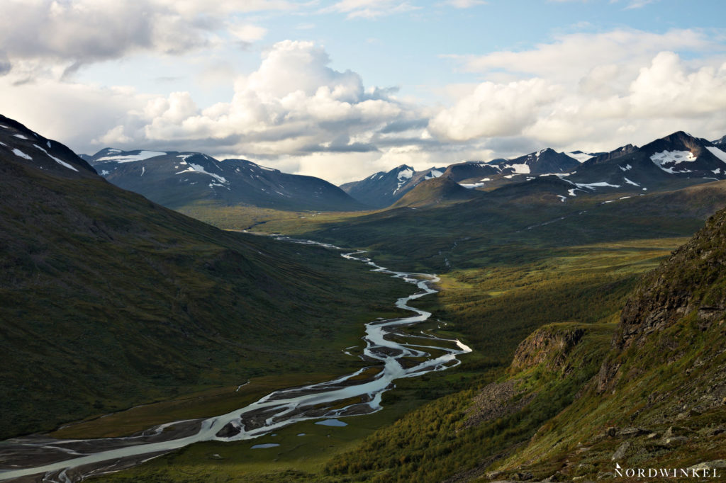 fluss windet sich durch grünes tal zwischen schneebedeckten gipfeln