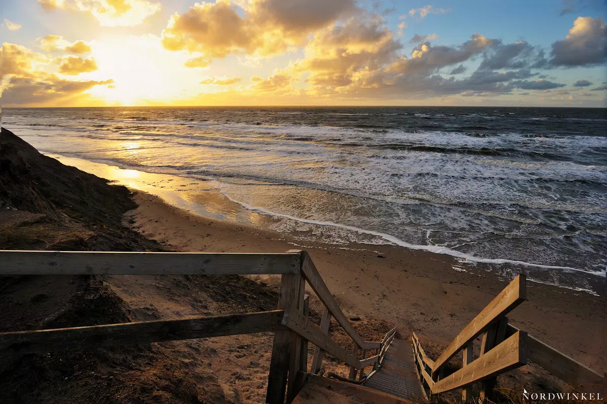 steile treppe führt zum strand mit schäumendem meer leicht bewölktem himmel zum sonnenuntergang