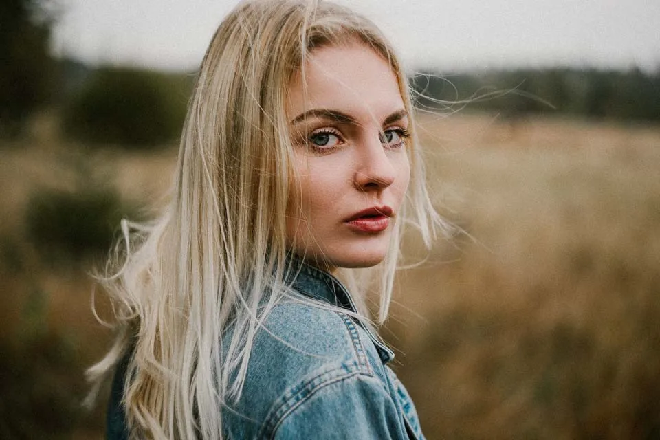 junge blonde frau blickt in der natur über ihre schulter zurück in die kamera