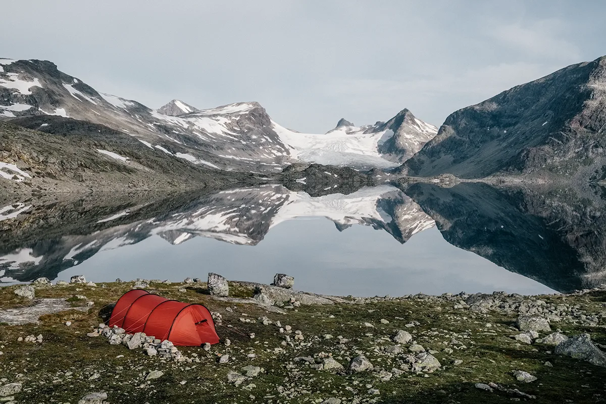 gebirgssee mit zelt im vordergrund und bergen im hintergrund
