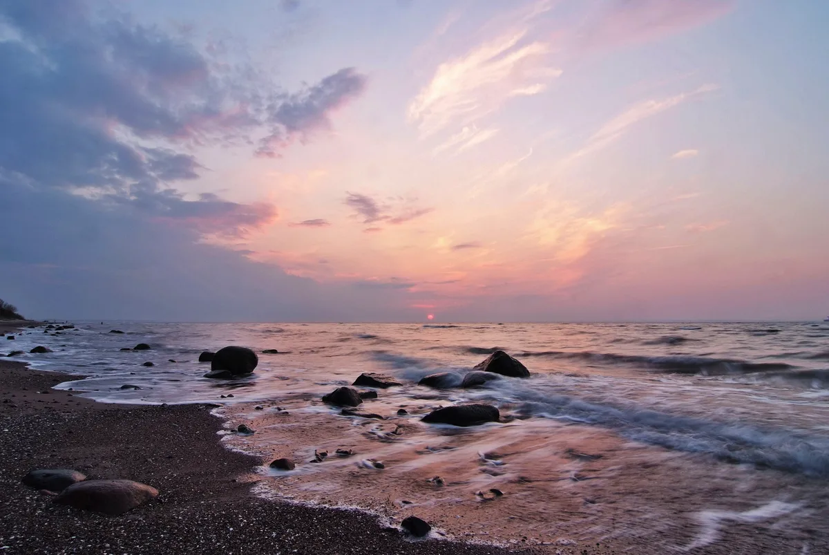 sonnenuntergang am meer mit steinigem strand und dunklen wolken