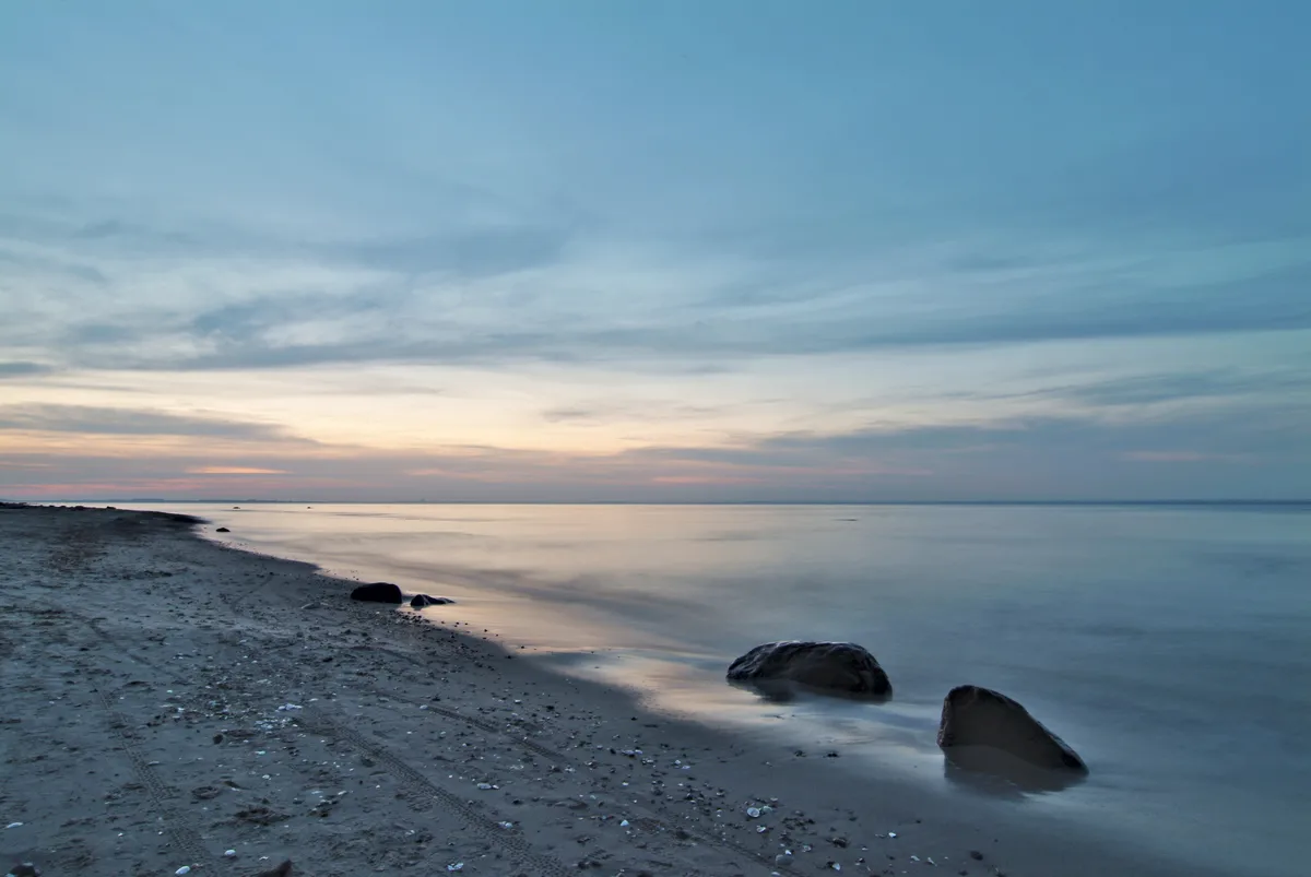 sonnenuntergang am ostseestrand mit blauem himmel und zwei steinen im vordergrund