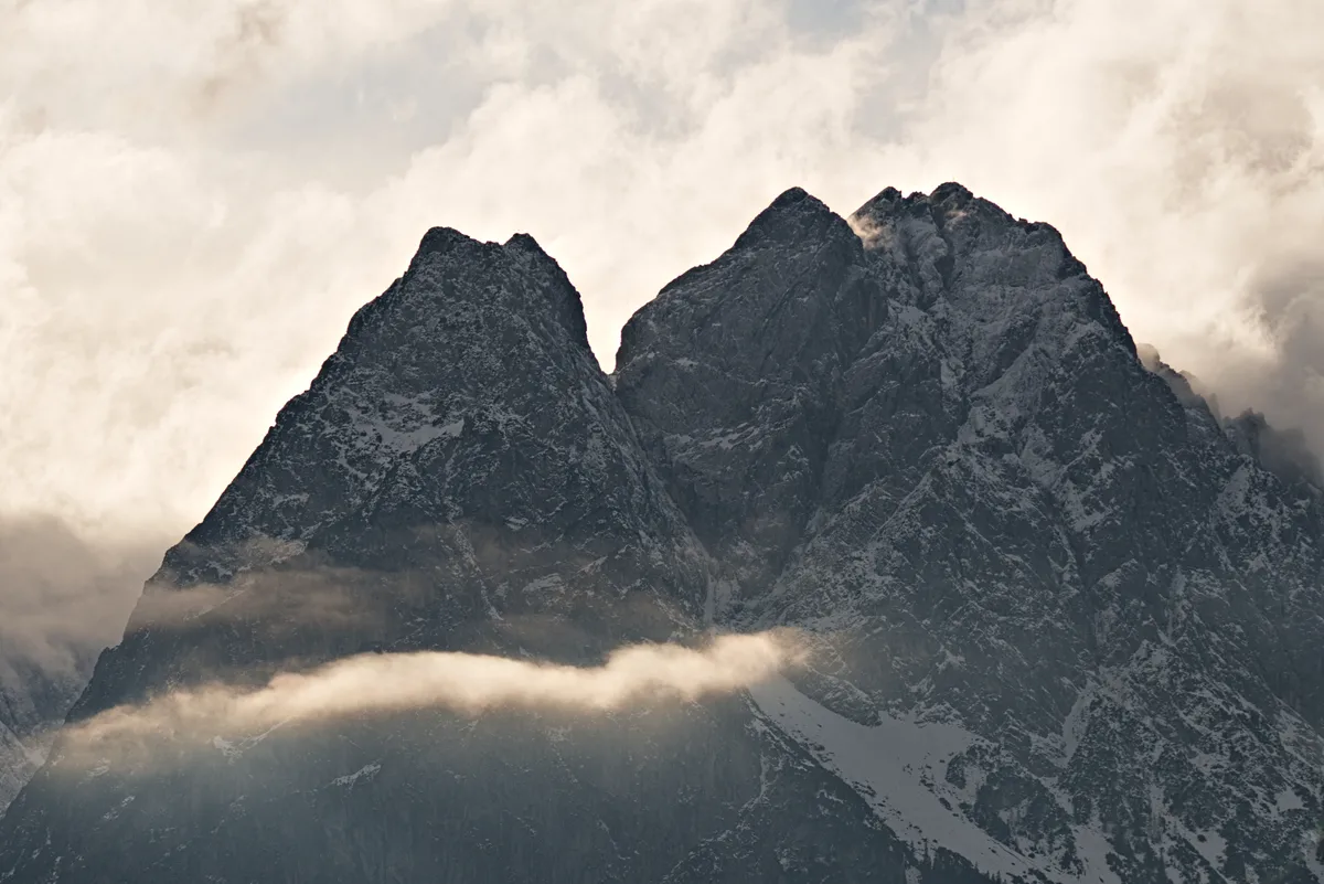 scharfkantige berggipfel vor leuchtenden wolken mit leuchtendem wolkenband vor gipfeln
