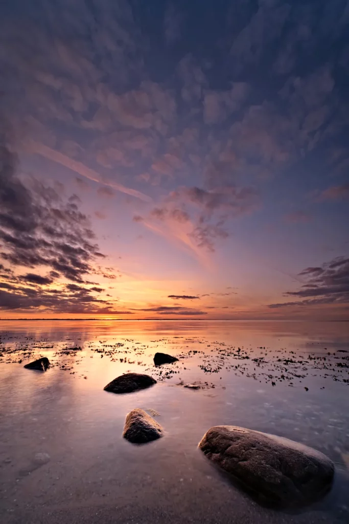 steine in glatter ostsee zum sonnenuntergang mit nahezu kompletten farbspektrum im himmel